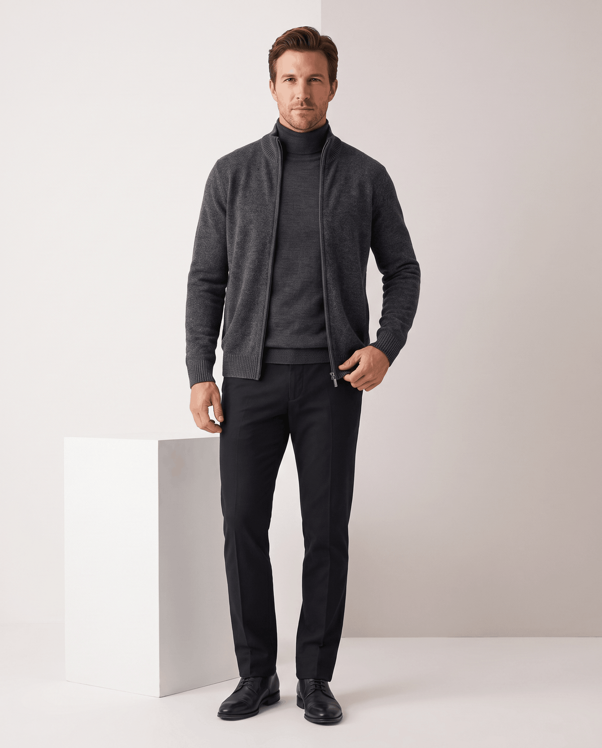 Man in a dark gray zip-up cardigan with black trousers and black shoes