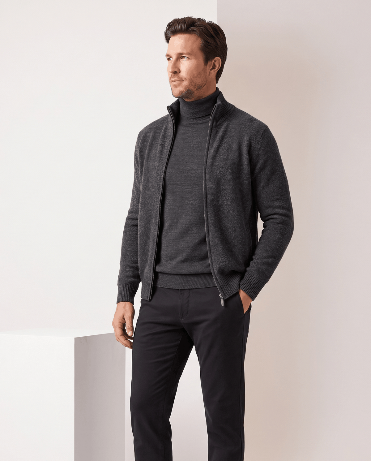 Dark gray zip cardigan worn open over a charcoal turtleneck and black trousers