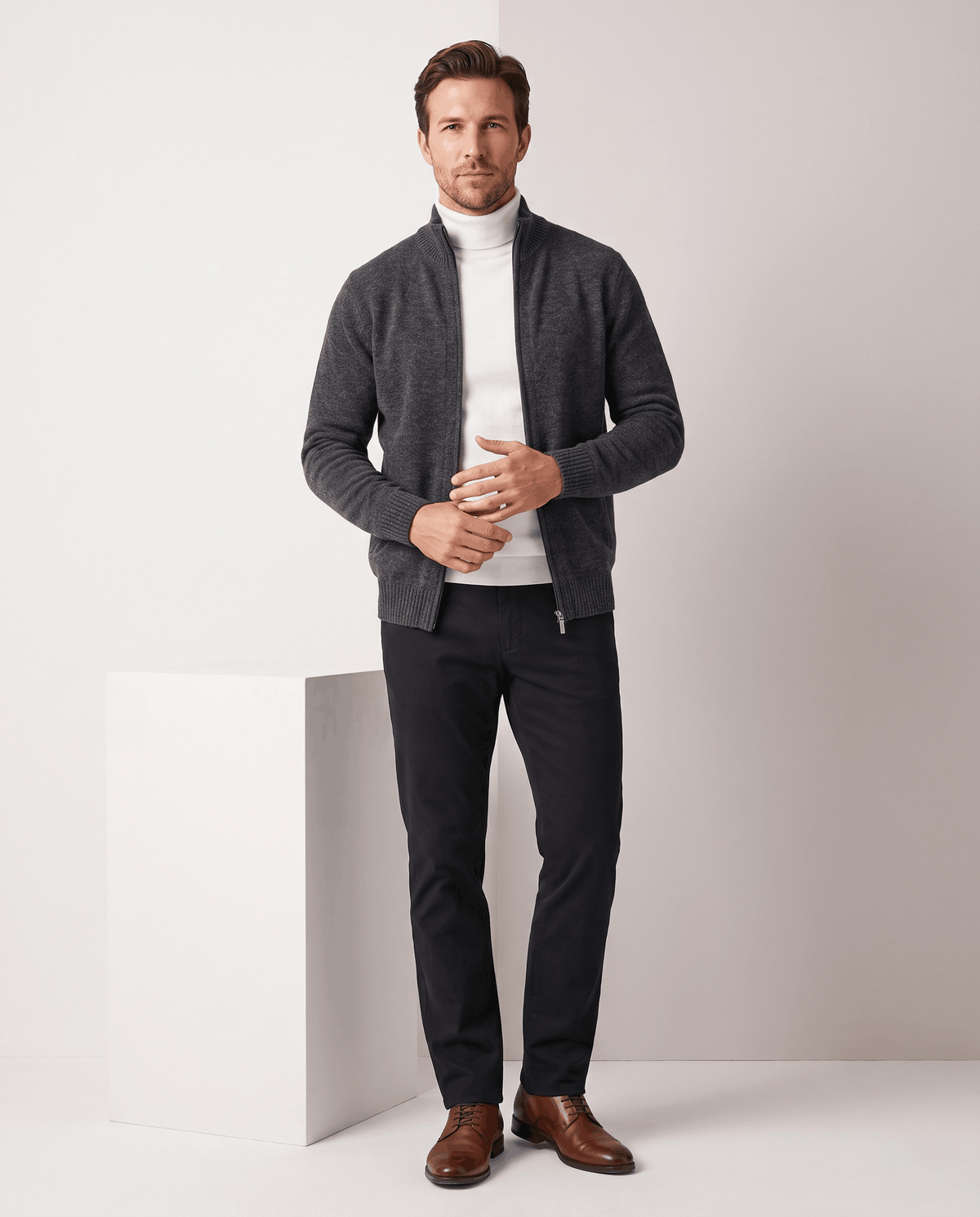 Dark gray cardigan styled over a white turtleneck with dark trousers and brown shoes