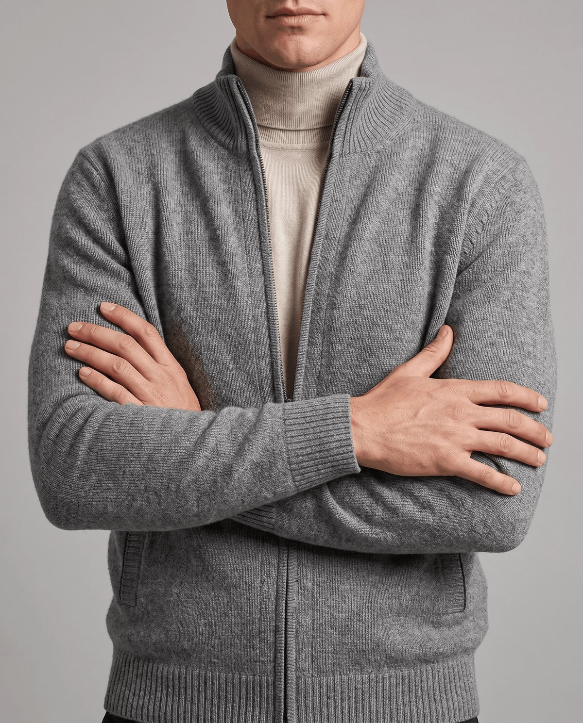 Arms crossed in a light gray zip cardigan layered over a cream turtleneck