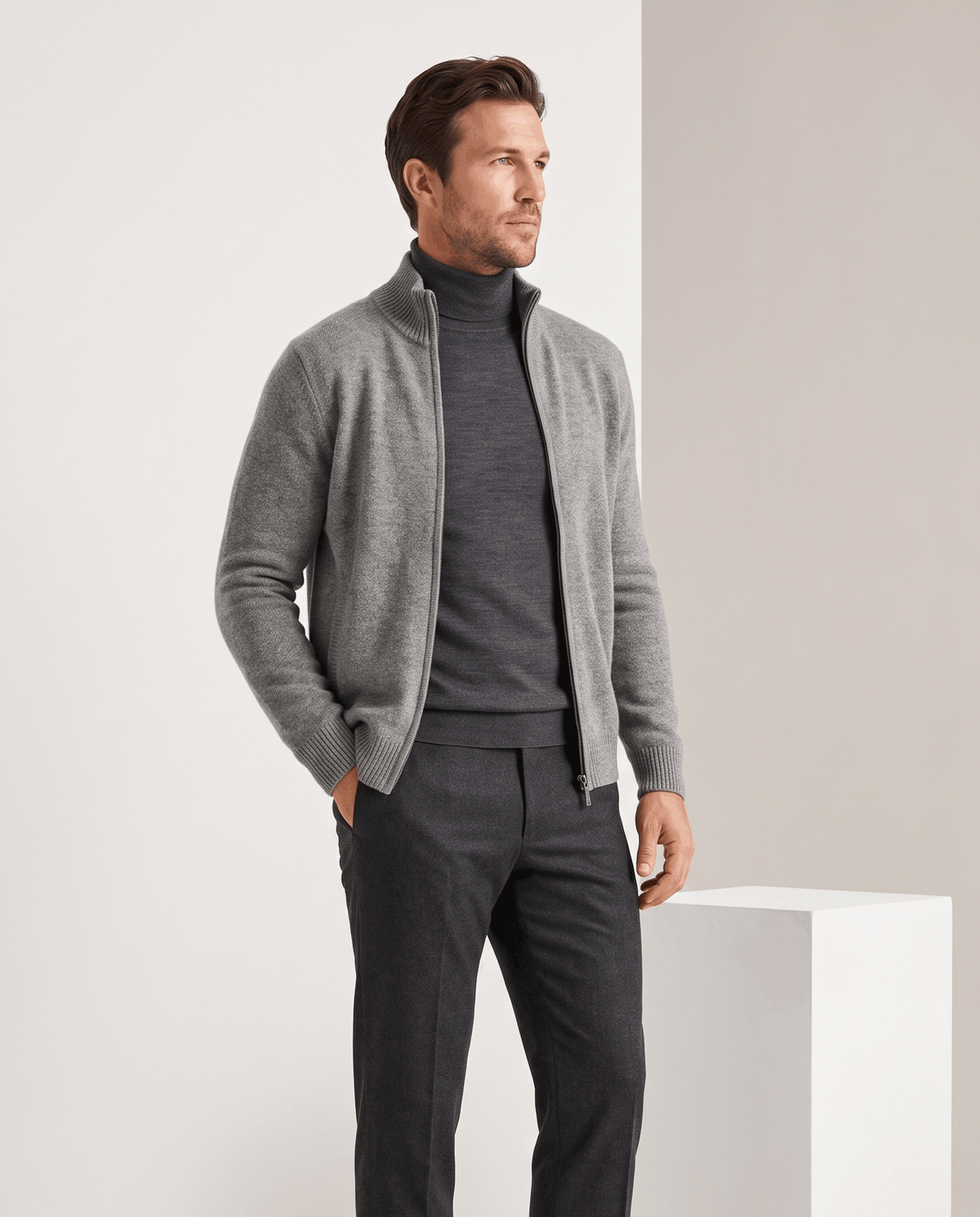 Light gray zip cardigan worn open over a charcoal turtleneck with one hand in pocket