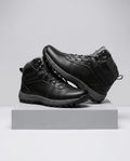 Black men's lace-up ankle boots with lug sole displayed on a grey studio plinth