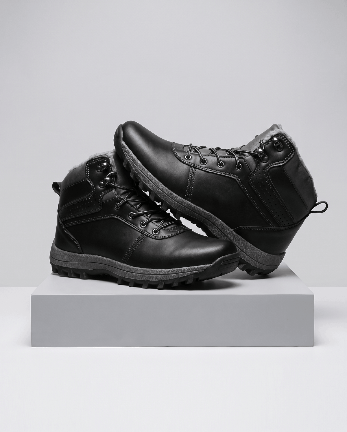 Black men's lace-up ankle boots with lug sole displayed on a grey studio plinth