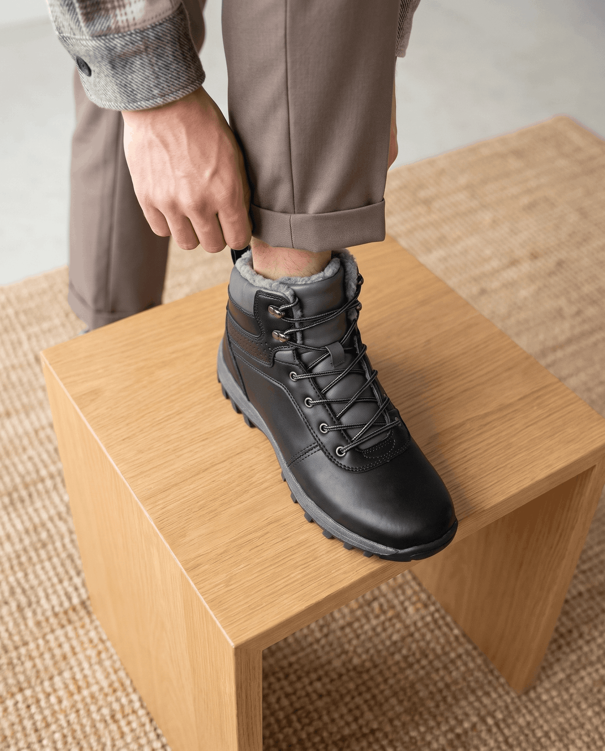 Man adjusting his trouser cuff over a black ankle boot on a wooden box