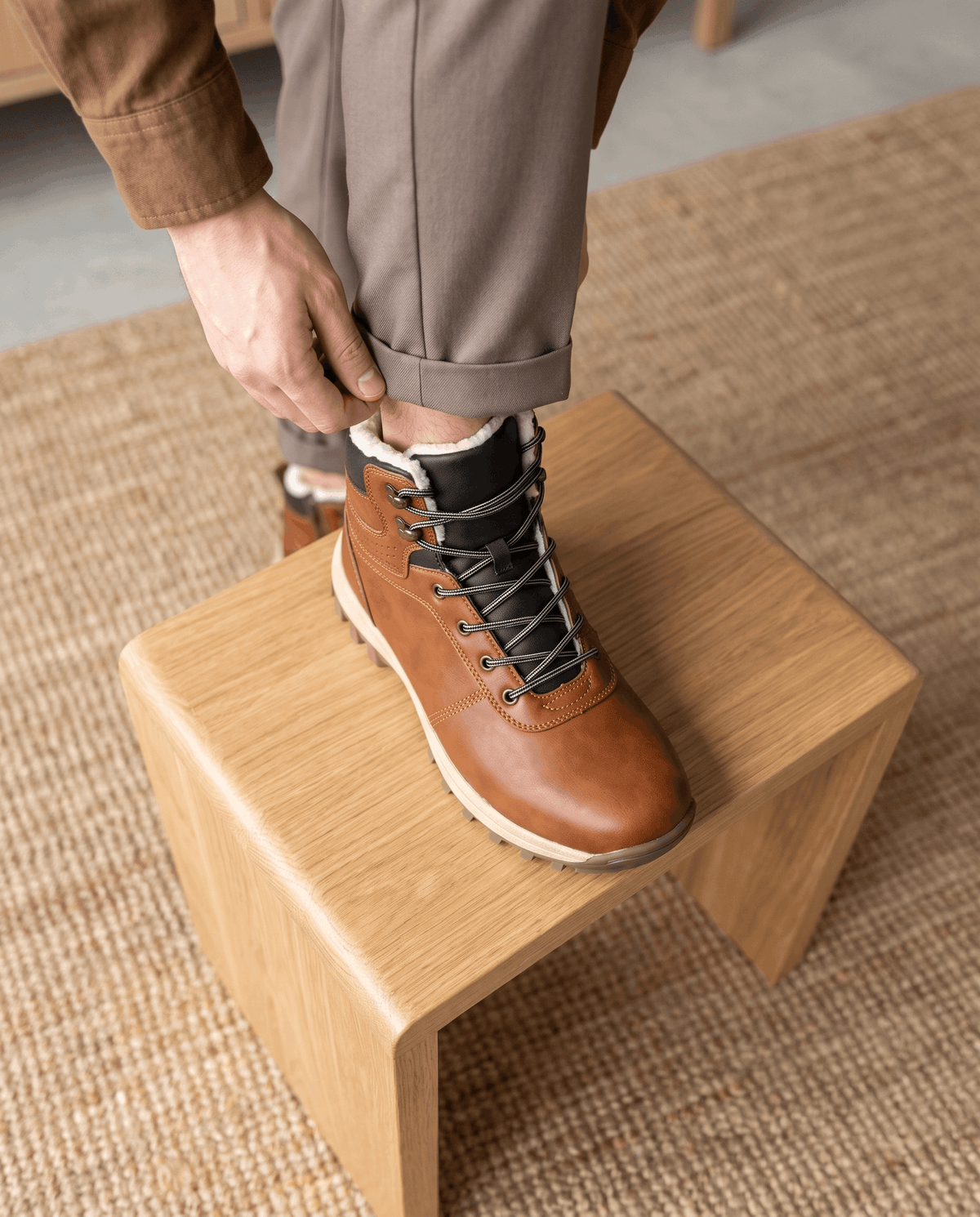 Close view of a hand pulling the laces tight at the top hooks of a brown boot