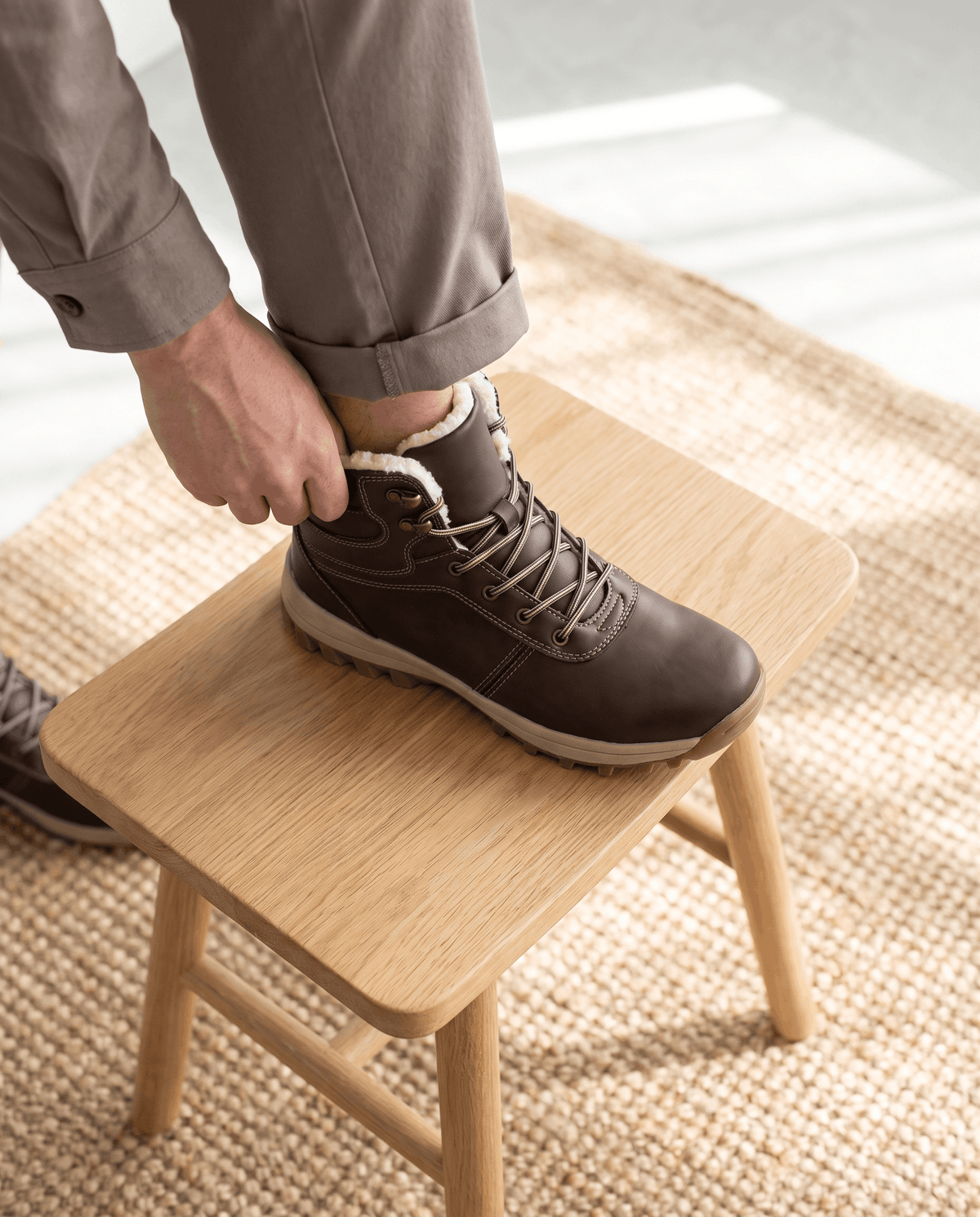 Hand lacing a dark brown boot resting on a pale oak bench in daylight