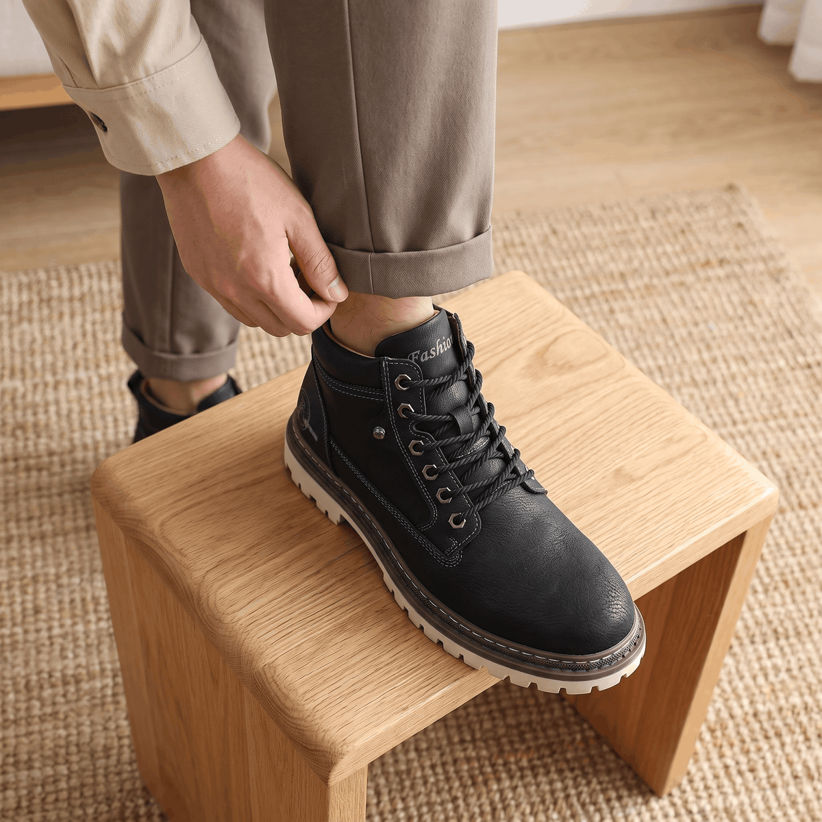 Black lace-up work boots with textured grain leather, bolt-style eyelets, and a chunky white lug sole resting on a wooden stool.