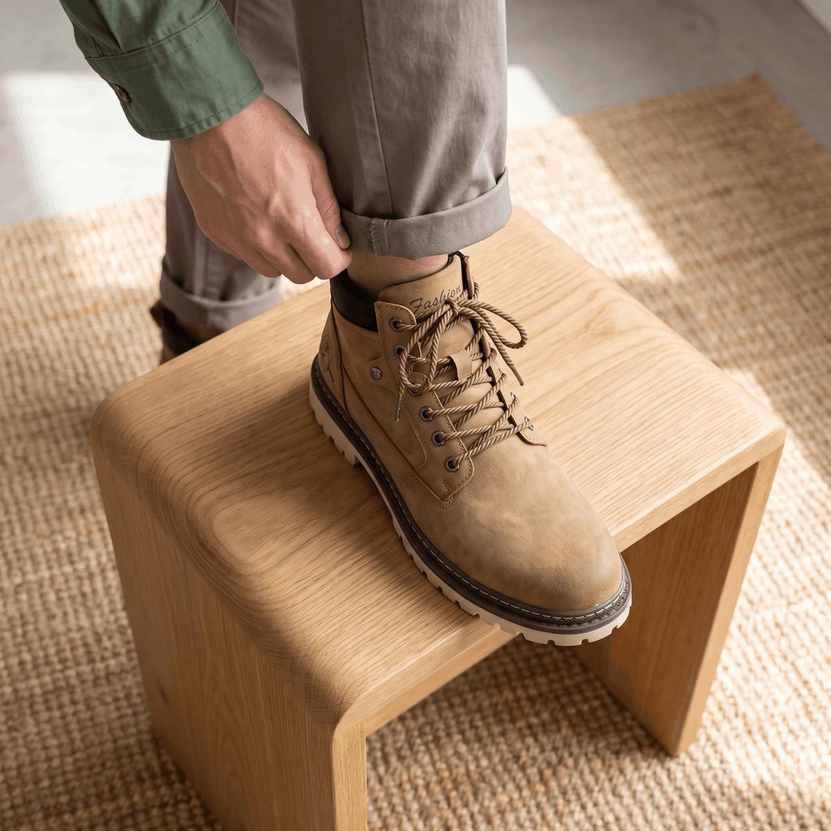 Khaki textured grain lace-up work boot with a padded collar, bolt-style eyelets, and a chunky lug sole resting on a stool.