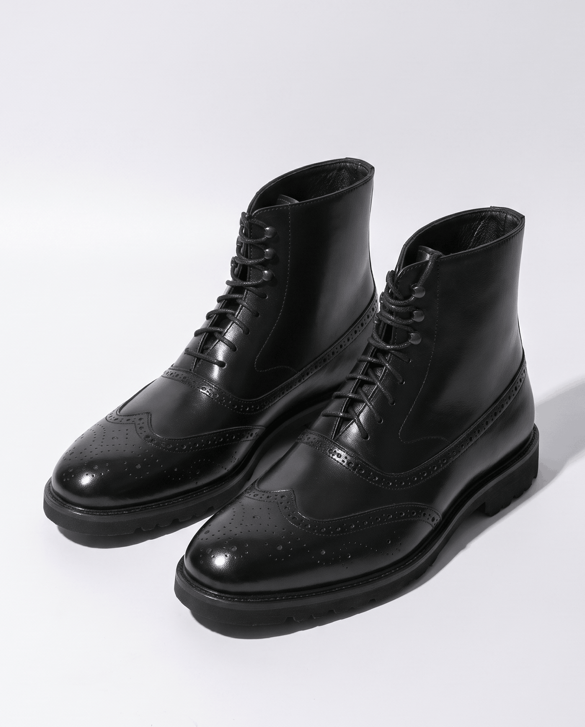 Pair of black brogue ankle boots with chunky soles on a light studio background