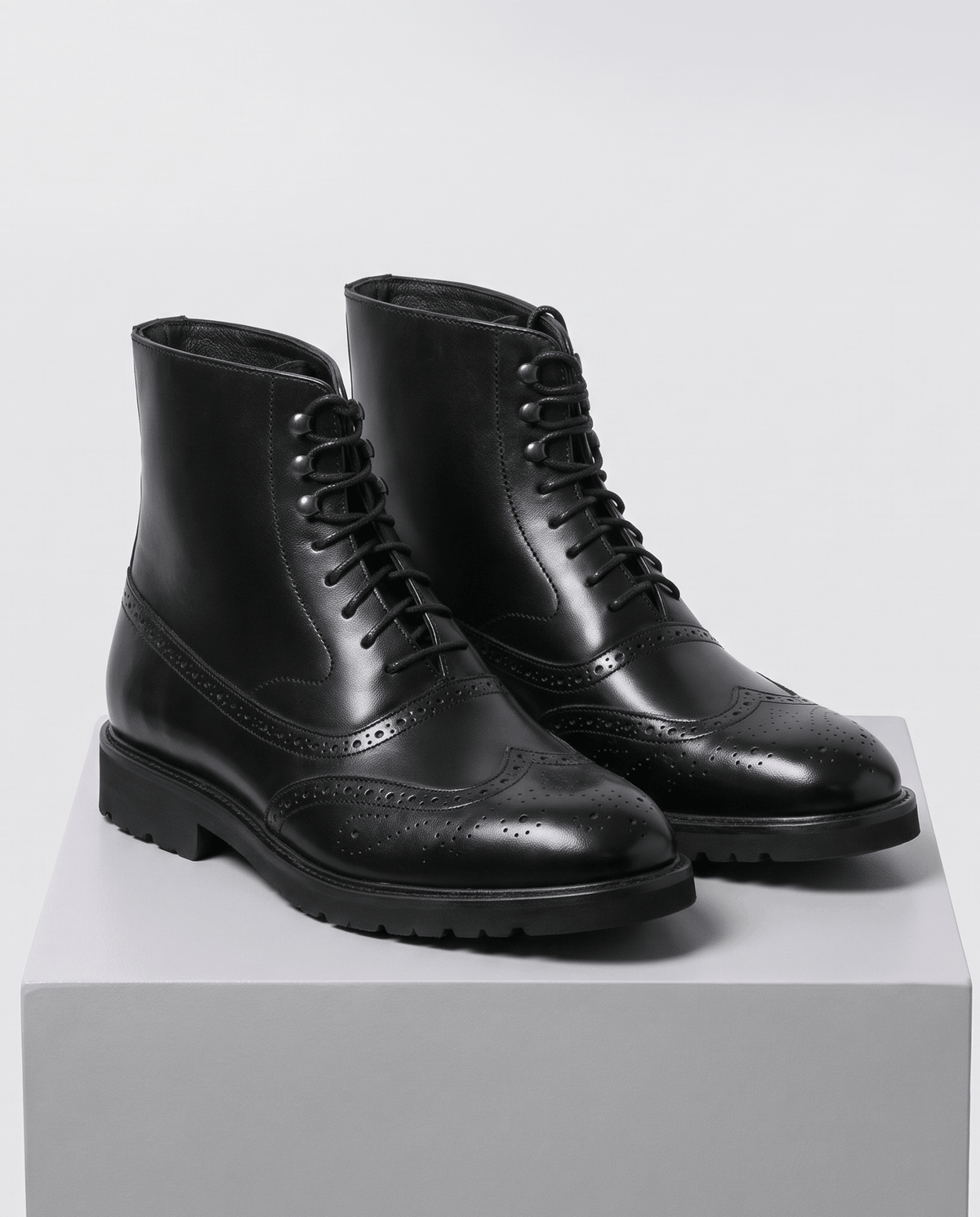 Black leather lace-up ankle boots shown as a pair on a gray plinth