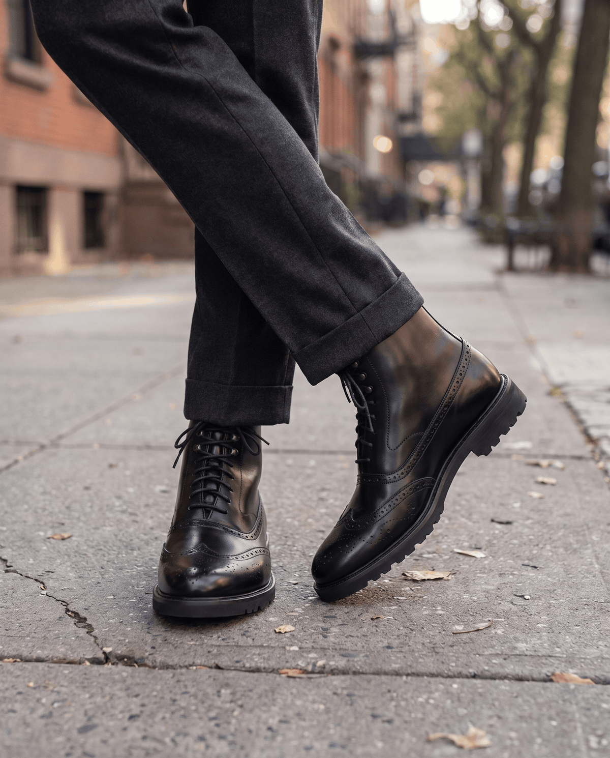 Man in black leather ankle boots and dark trousers walking along a city sidewalk