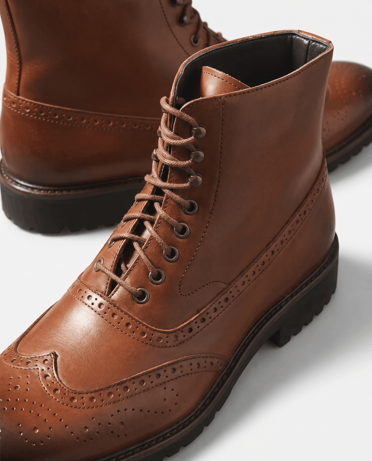 Close-up of brown brogue toe cap perforations and lace-up front on a leather ankle boot