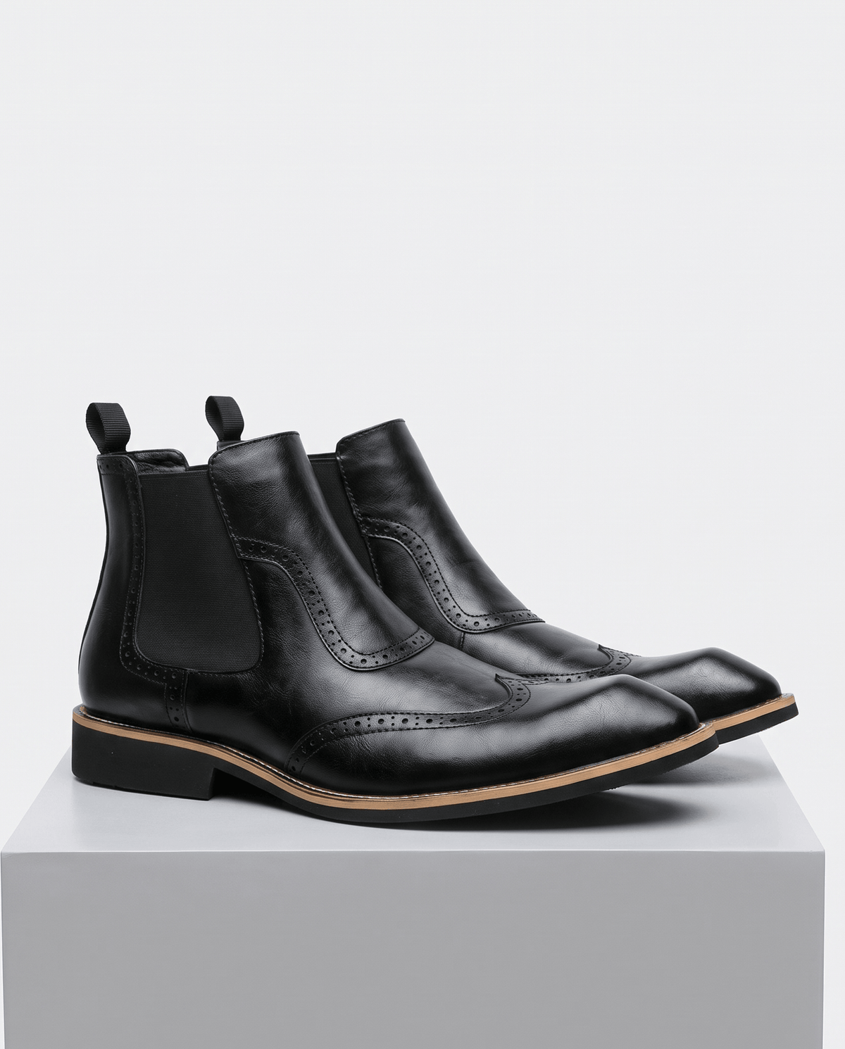 Men's black leather Chelsea boots with brogue detailing, shown as a pair on a gray block
