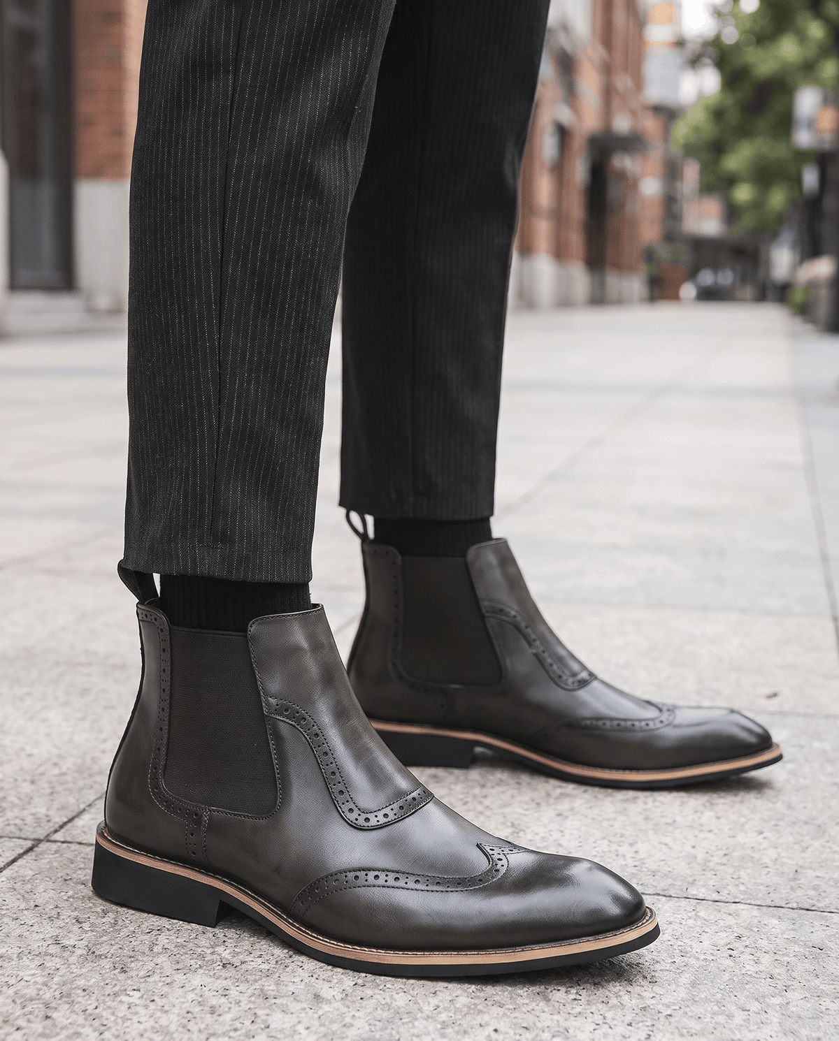 Man in black slip-on brogue boots and dark trousers standing on a paved street