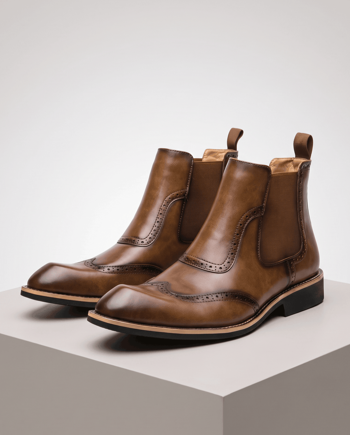 Pair of tan brown brogue Chelsea boots on a gray block