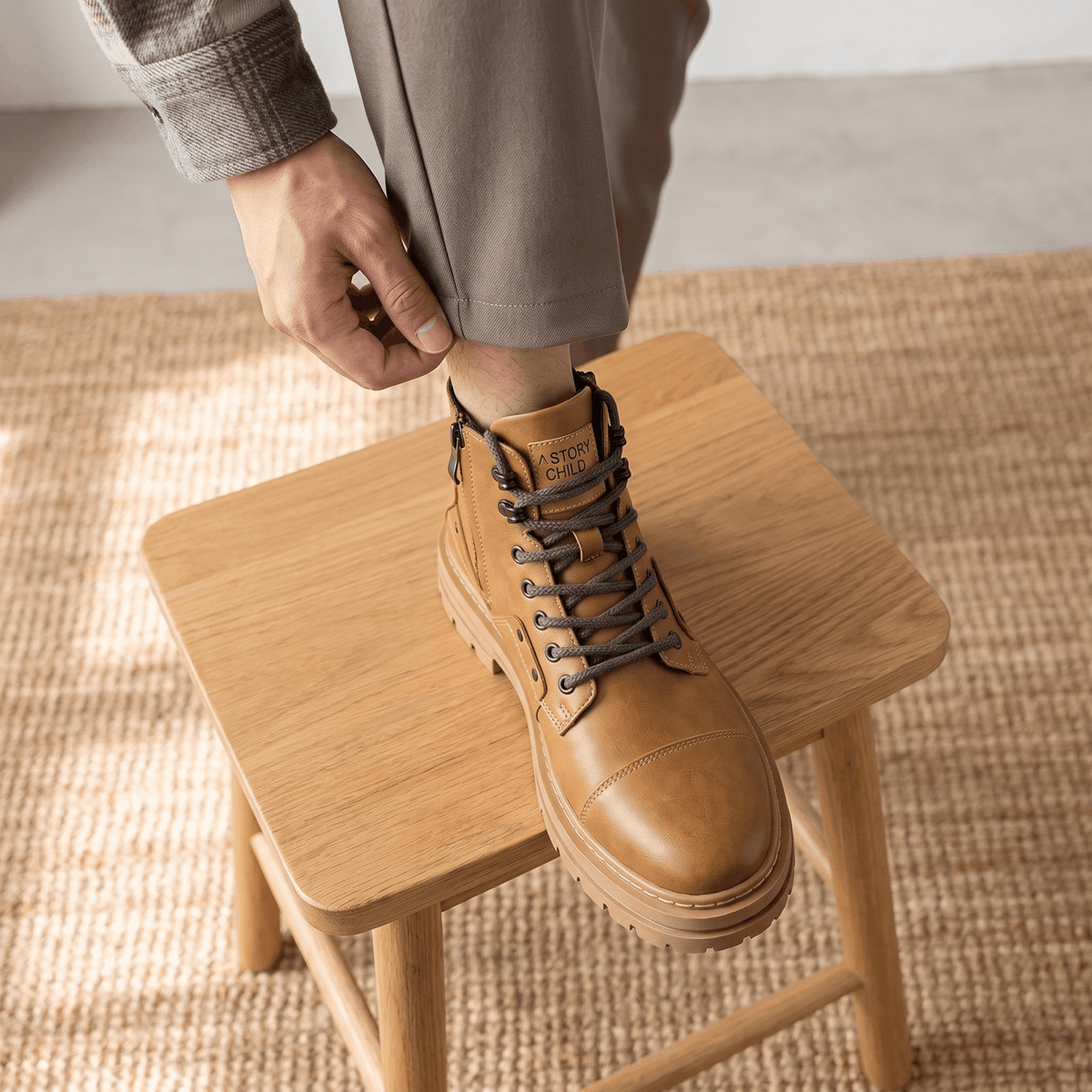 Tan leather combat boots with a reinforced cap toe, side zip, and thick lug sole resting on a wooden stool.