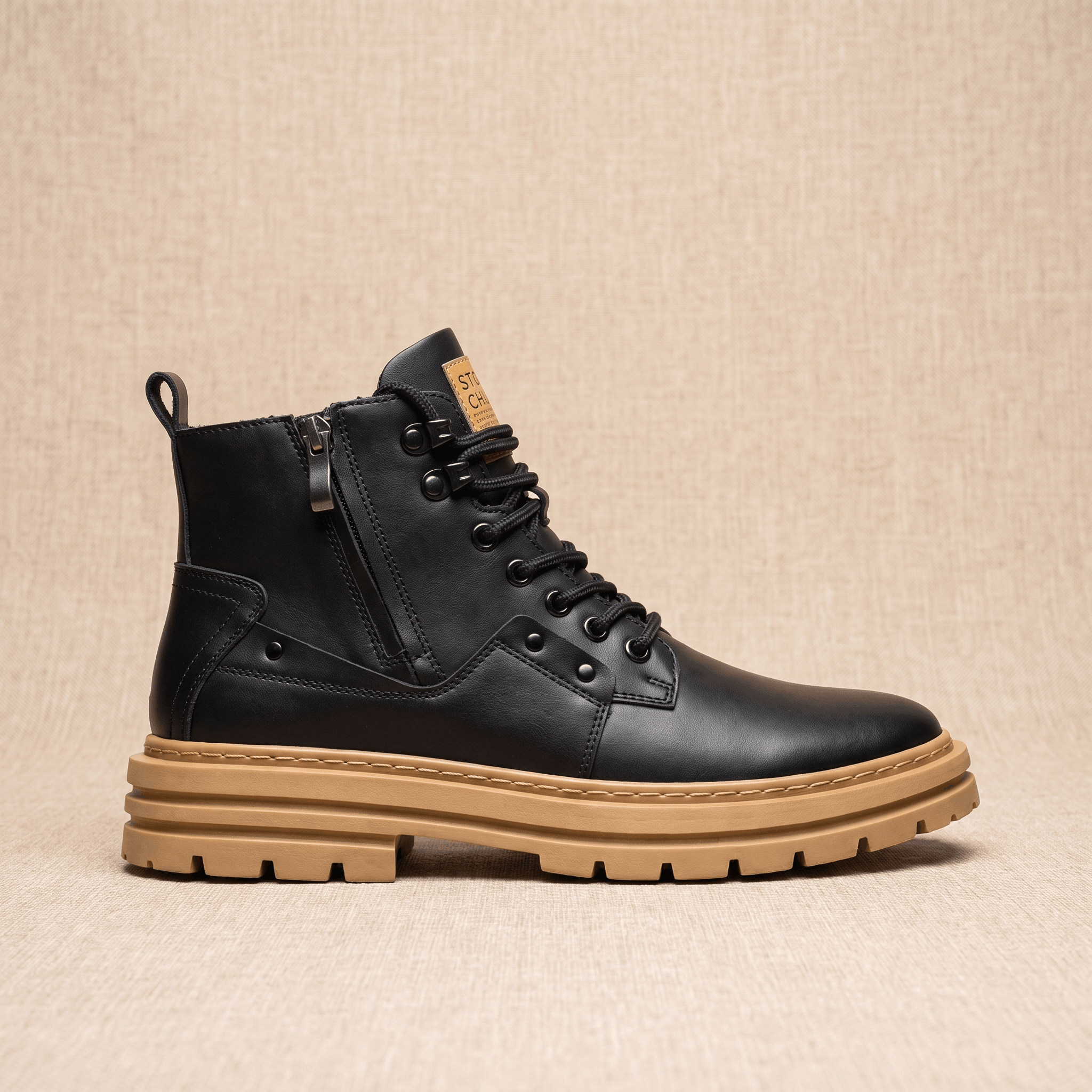 Black leather combat boot with side zip, lace-up front, and a chunky tan lug sole on a neutral textured background.