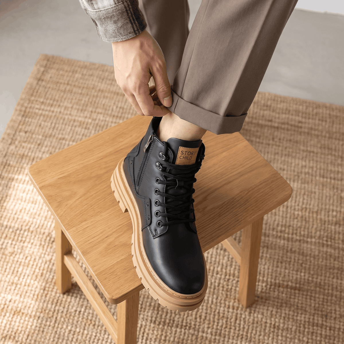 Black leather combat boots with a tan lug sole, side zip, and reinforced cap toe, worn with cuffed trousers.
