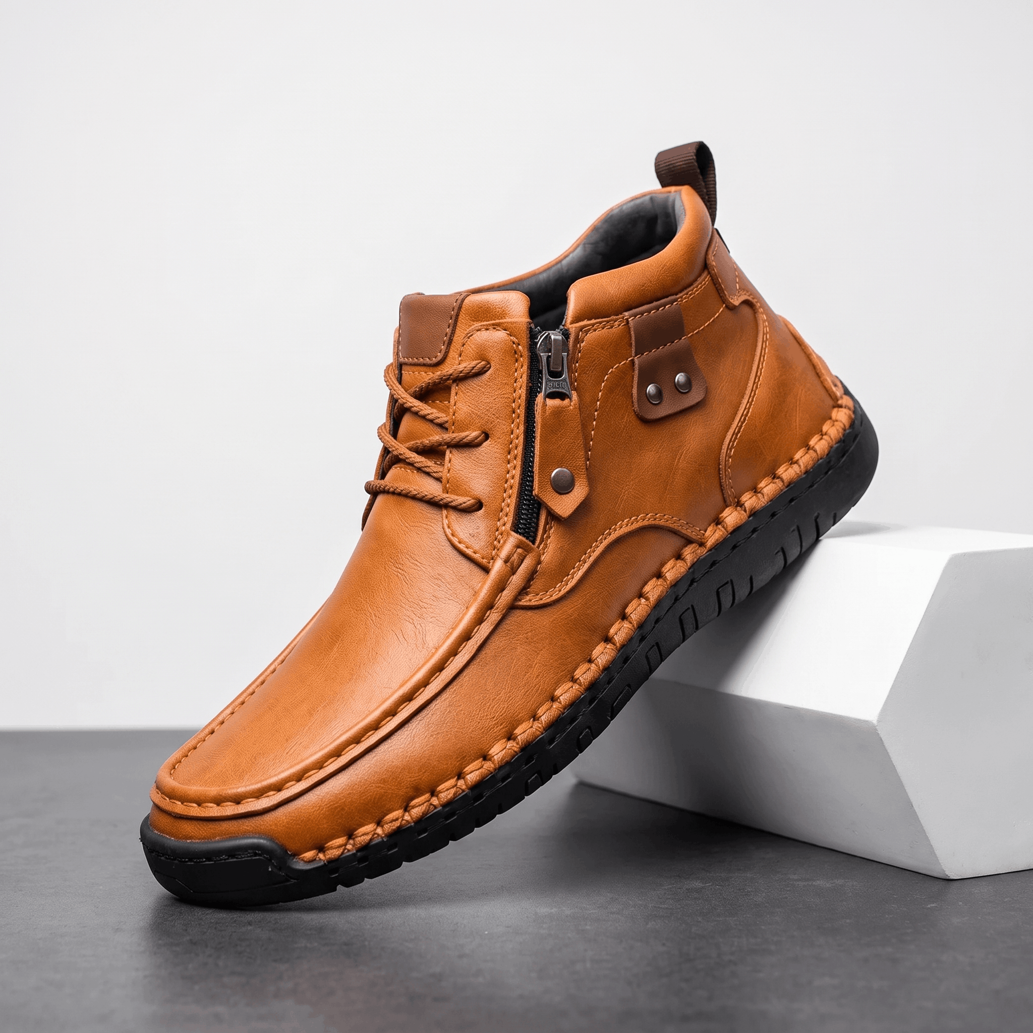 Brown leather moc toe boot with side zip, whipstitched rubber midsole, and apron seam detail on a white display block.