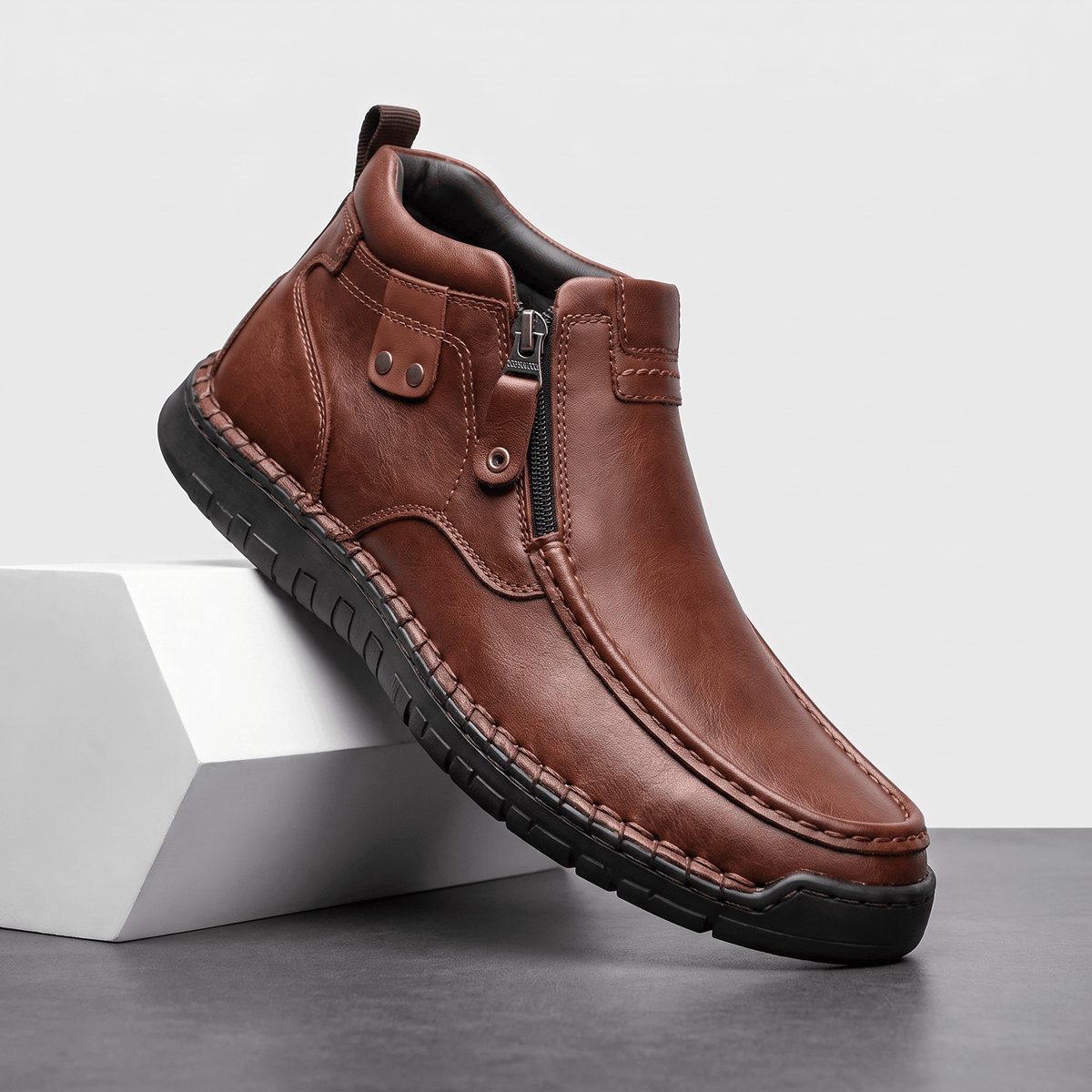 Dark brown leather moc toe boot with side zip, apron seam, and black rubber whipstitched midsole on a white block.