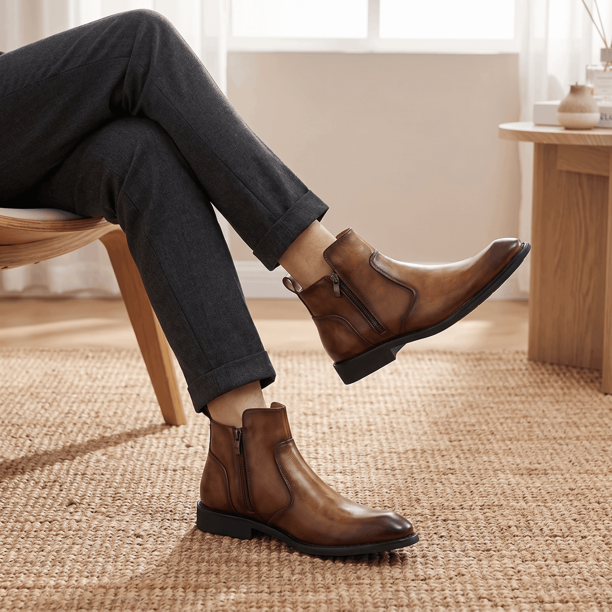 Burnished brown leather dress boots with a pointed toe, inside zip closure, and low stacked heel worn with grey trousers.