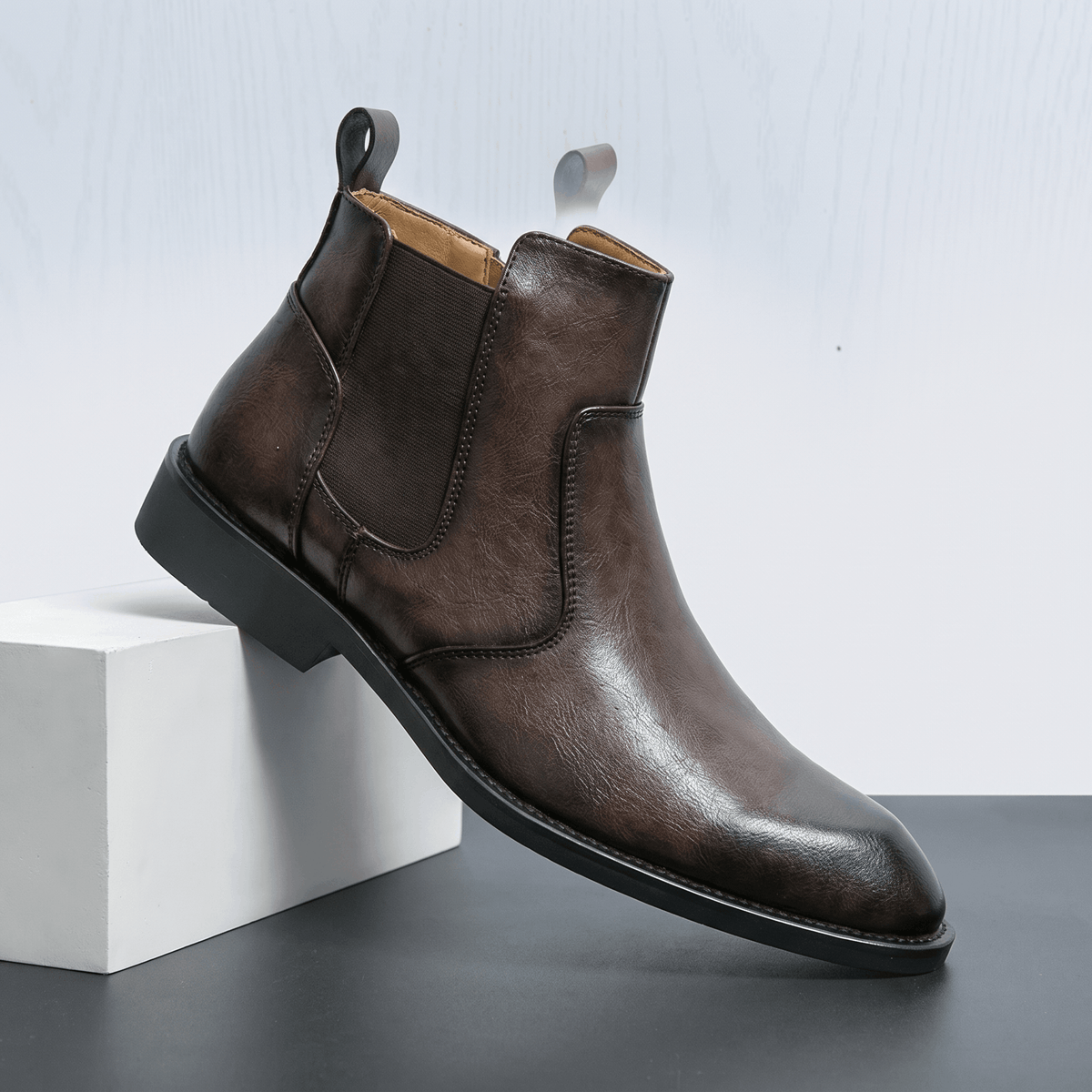 Burnished dark brown leather dress boot with a pointed toe, slim stacked heel, and inside zip closure on a white block.