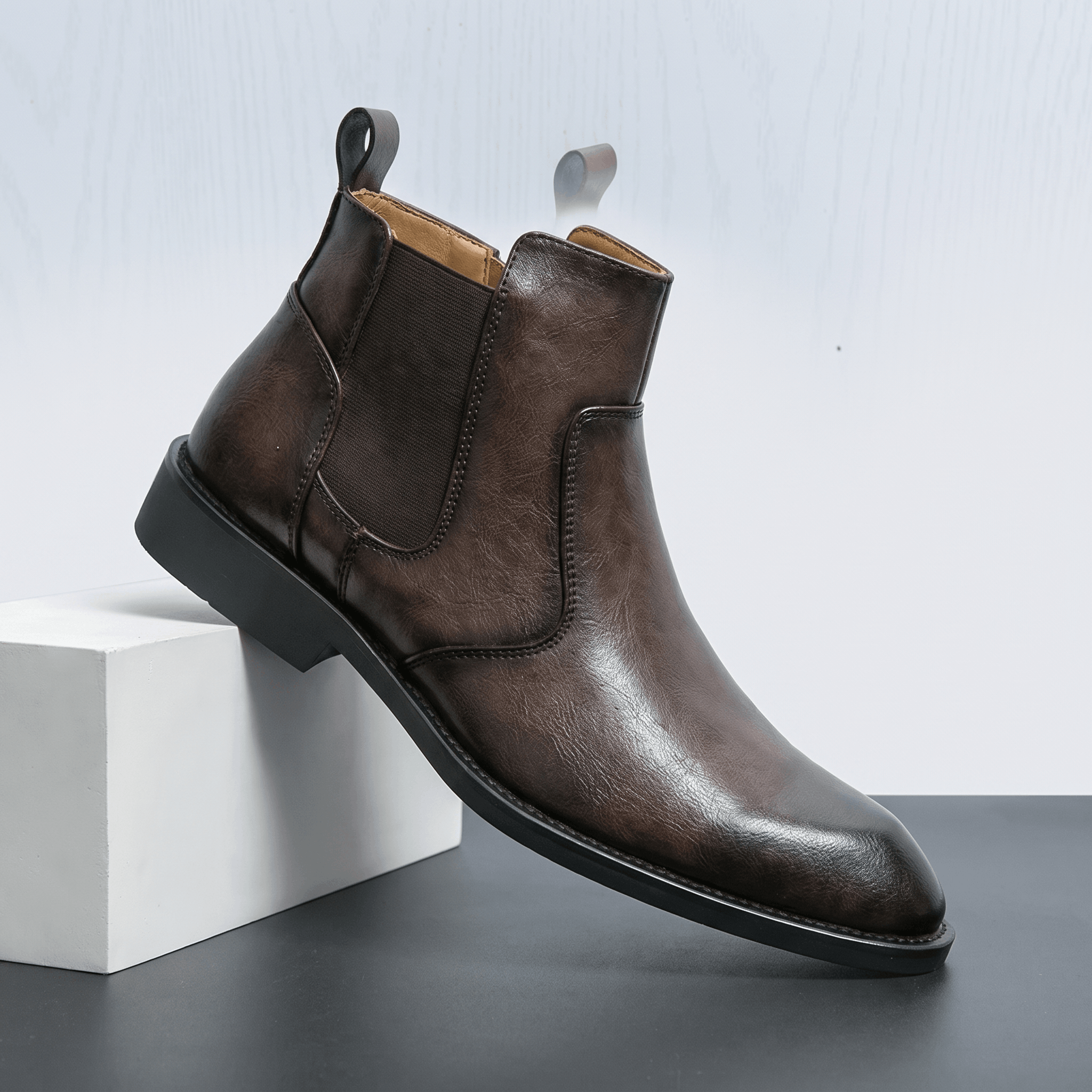 Burnished dark brown leather dress boot with a pointed toe, slim stacked heel, and inside zip closure on a white block.