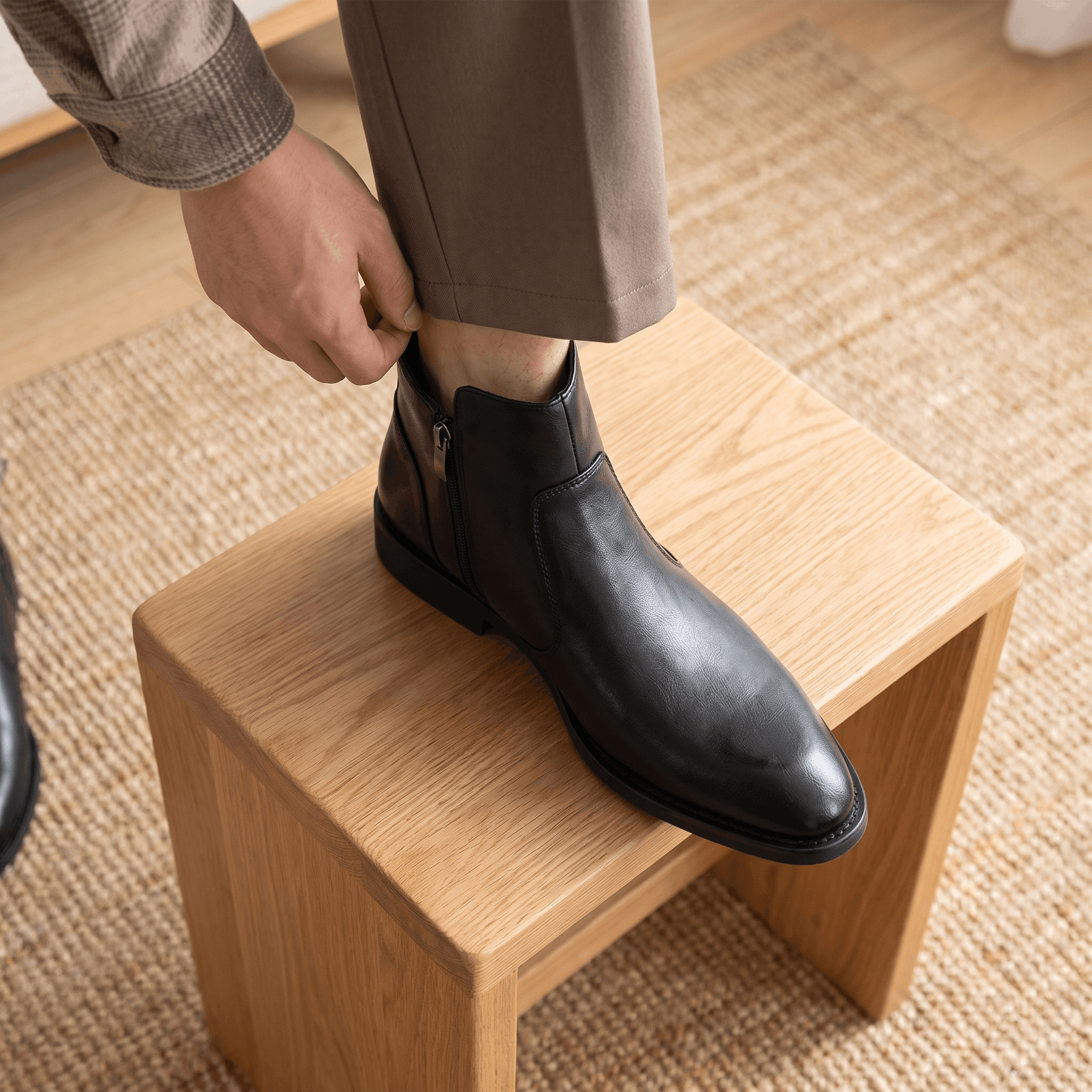 Black burnished leather dress boot with a pointed toe, inside zip closure, and low stacked heel worn with trousers.
