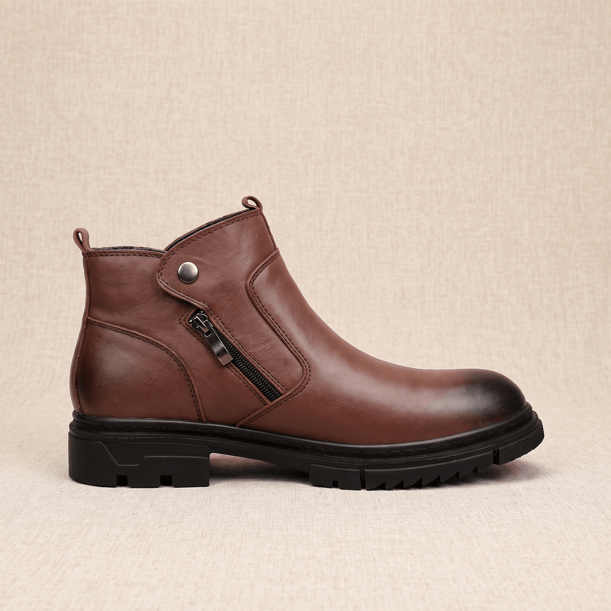Smooth brown leather ankle boot with a side zip, snap tab detail, and a chunky black lug sole on a textured background.