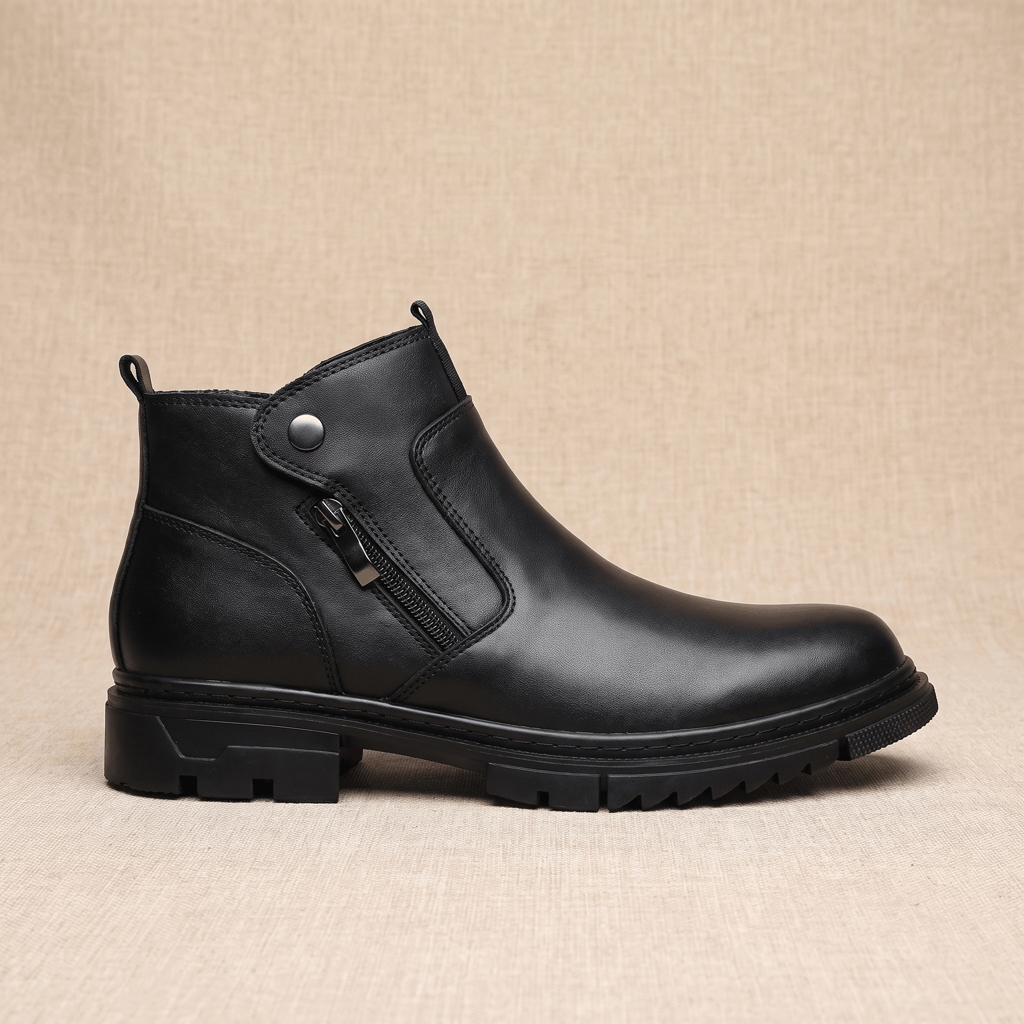 Black leather ankle boot with side zip, snap tab detail, and a chunky lug rubber outsole on a neutral background.
