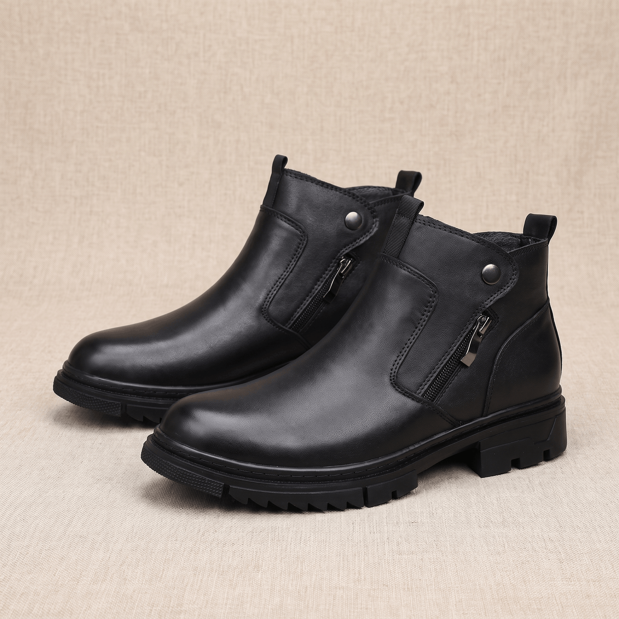 Black leather ankle boots with side zip, snap tab detail, and a chunky lugged rubber sole on a neutral textured background.