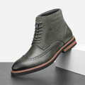 Gray leather wingtip ankle boot with a suede shaft panel, brogue detailing, burnished toe, and a stacked welted rubber sole.