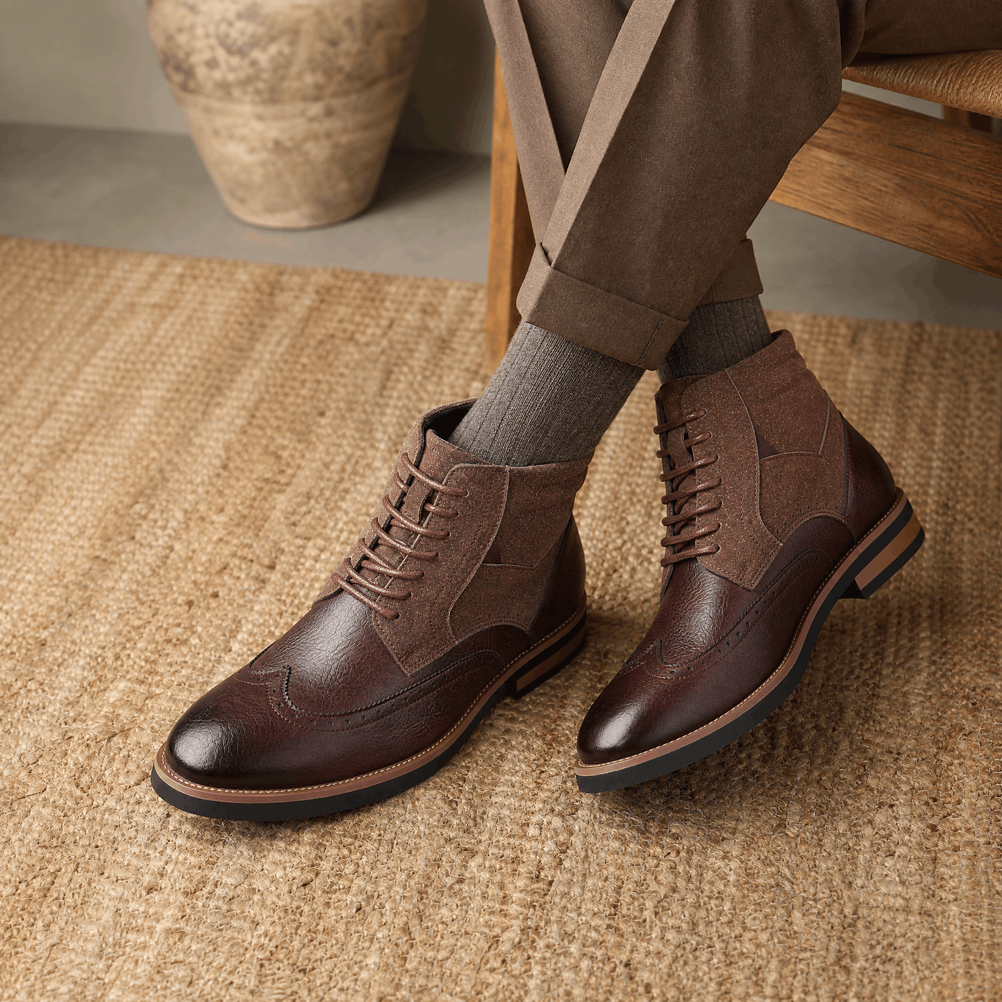 Dark brown leather wingtip ankle boots with suede shaft panels, burnished toes, and welted rubber soles worn with trousers.