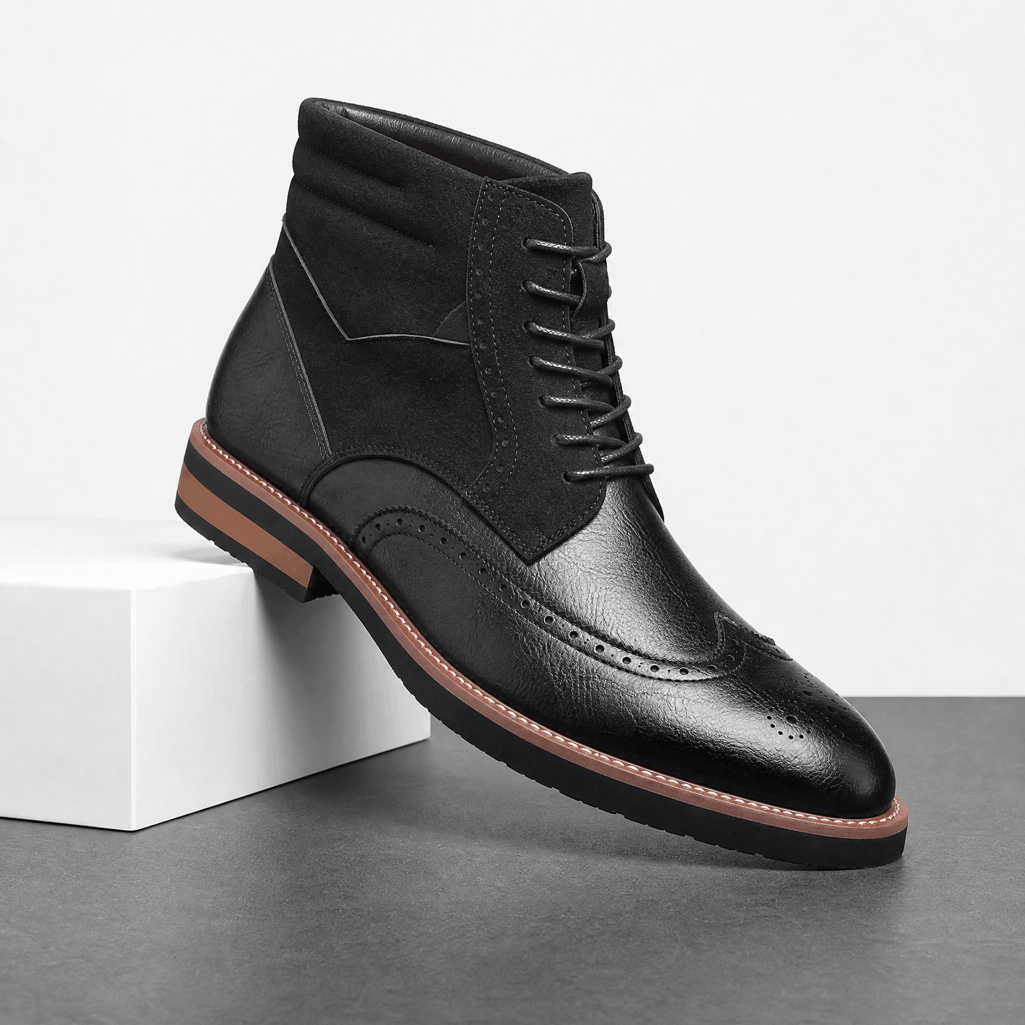 Black leather wingtip brogue ankle boots with a suede shaft panel, lace-up front, and a contrast welted rubber sole.