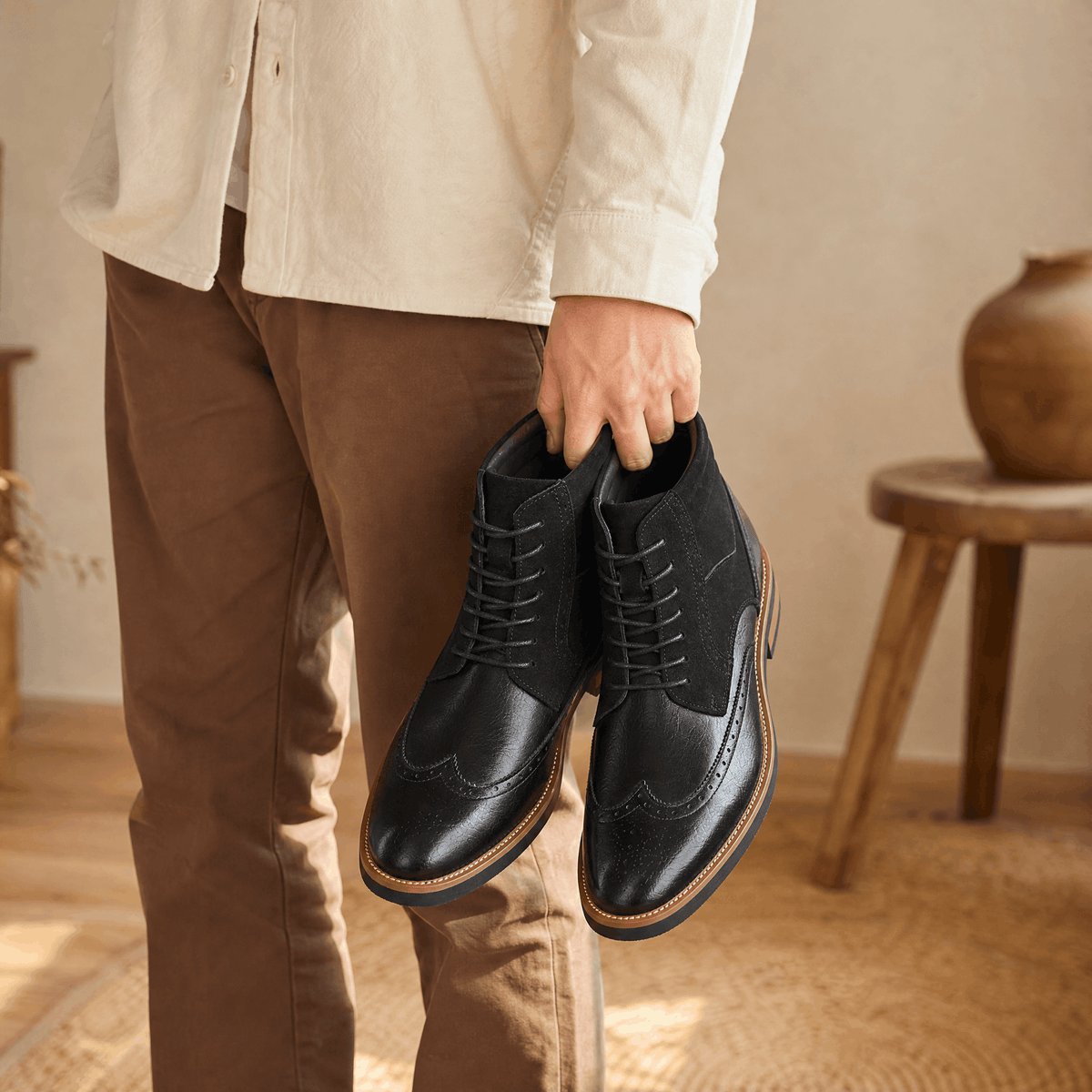 Black leather wingtip ankle boots featuring a suede shaft, lace-up closure, and a durable welted rubber sole.