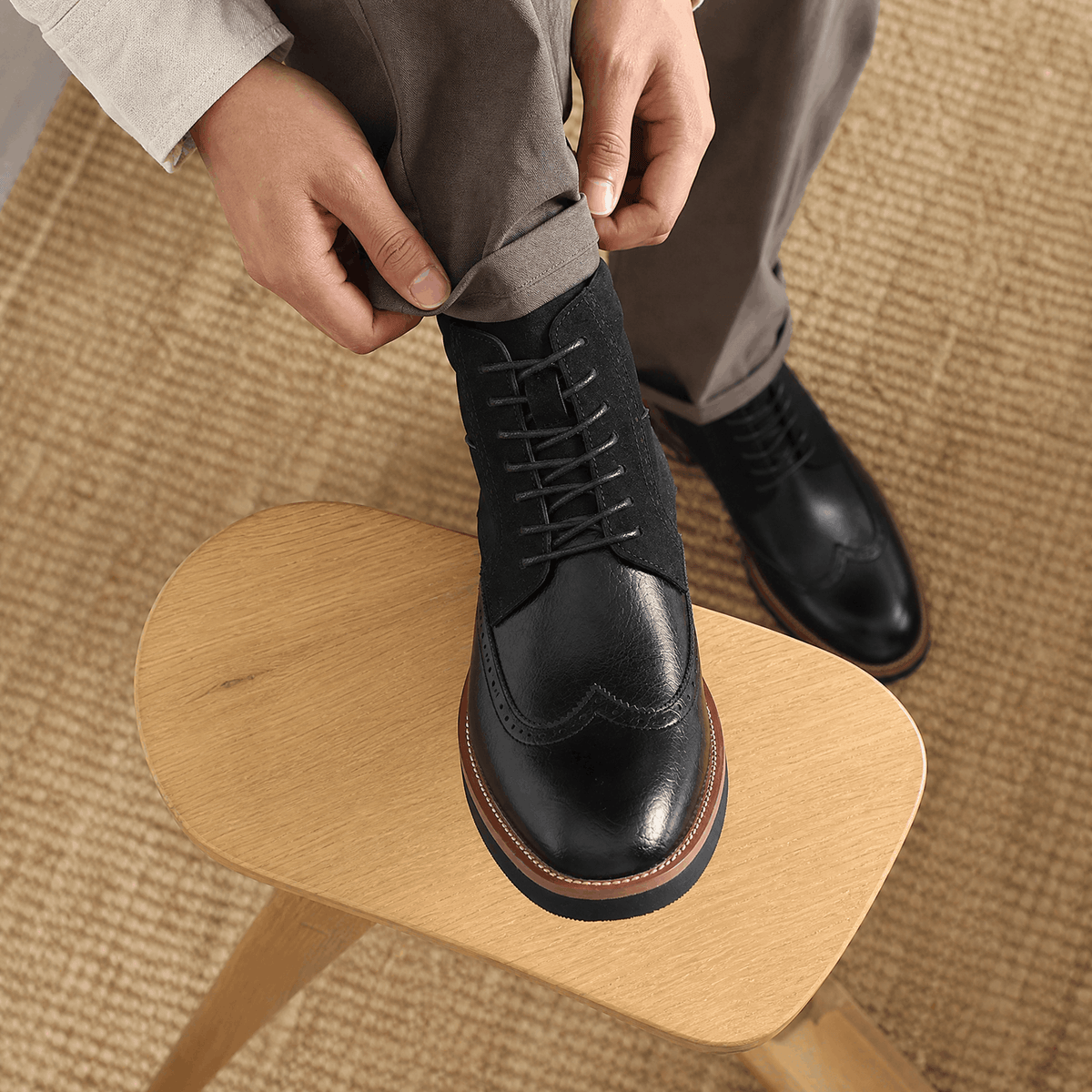 Black leather wingtip ankle boots featuring a suede shaft panel, lace-up closure, and a welted rubber sole.