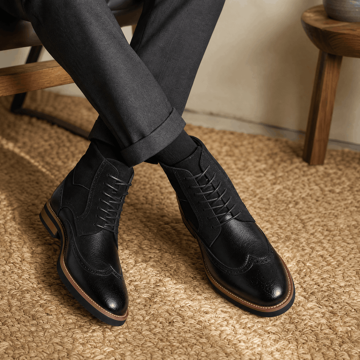 Black leather wingtip brogue ankle boots with suede shaft panels, lace-up closure, and a welted rubber sole.