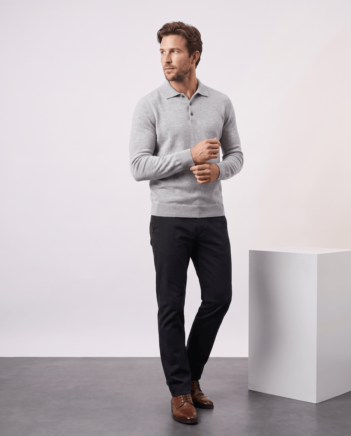 Full-length view of a man wearing the Elias light gray polo sweater with dark trousers
