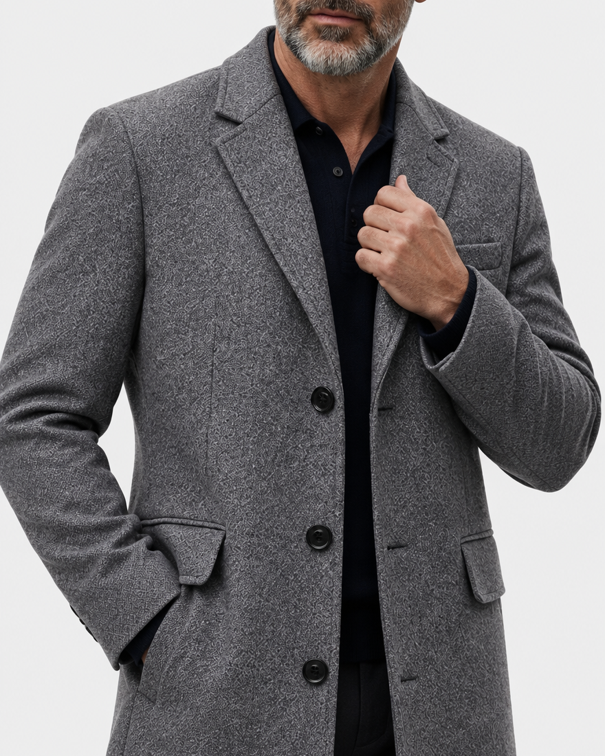 Close-up of the gray coat's notch lapel, button front and flap pocket with a hand at the collar