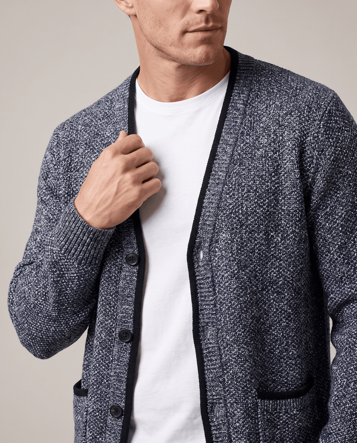 Hand at the black-trimmed placket of a blue cardigan over a white tee