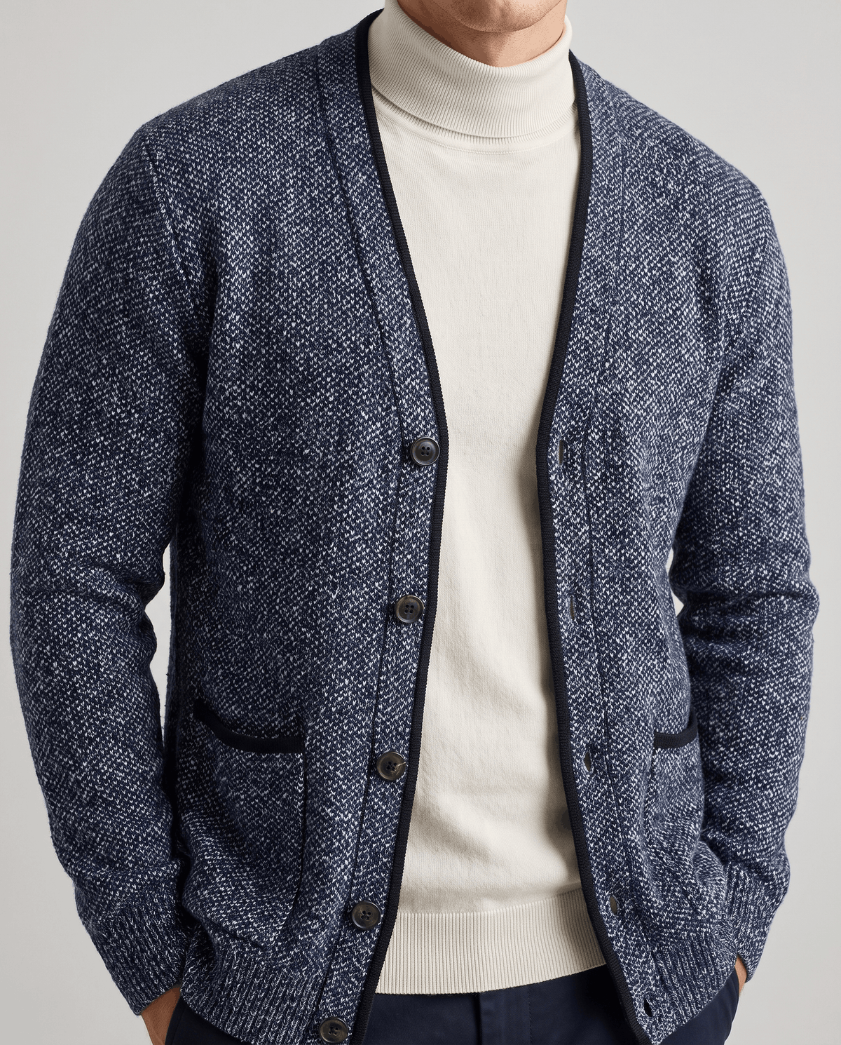Blue marled cardigan with hands in the pockets over a cream turtleneck