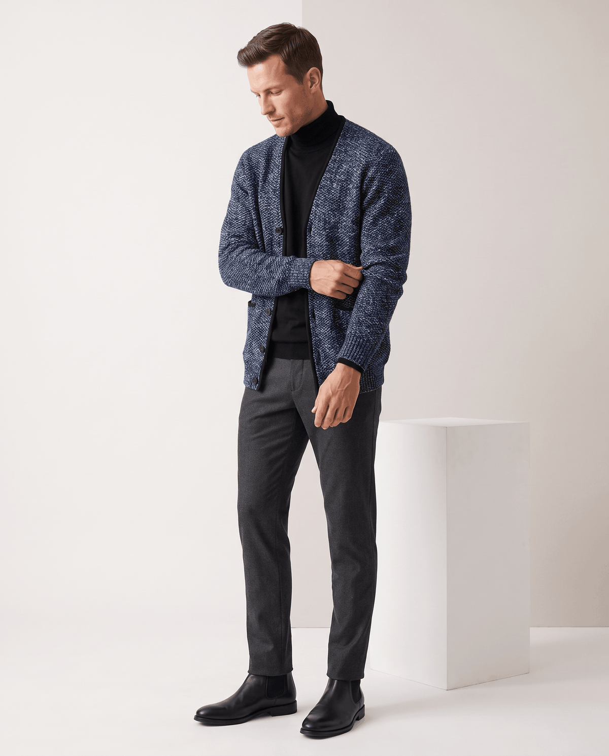 Blue cardigan over a black turtleneck with gray trousers and black shoes