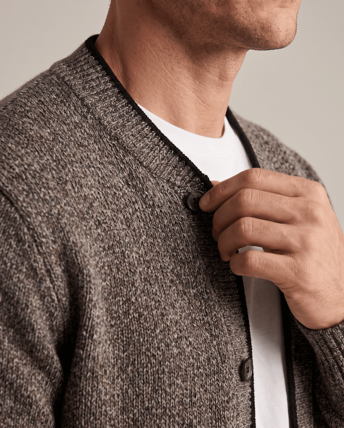 Hand at the button placket of a brown marled cardigan over a white tee