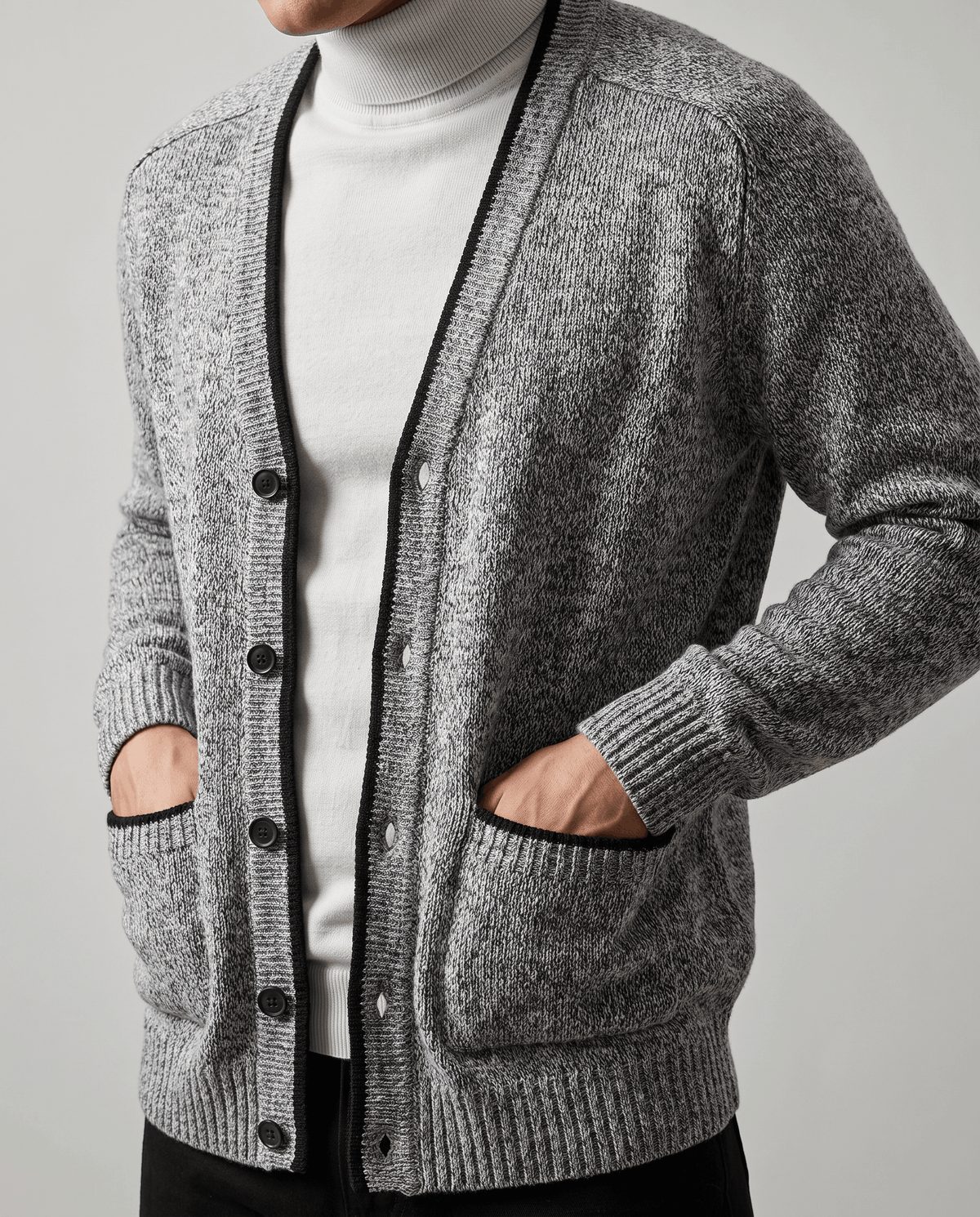 Hands in the black-trimmed pockets of a light gray marled cardigan