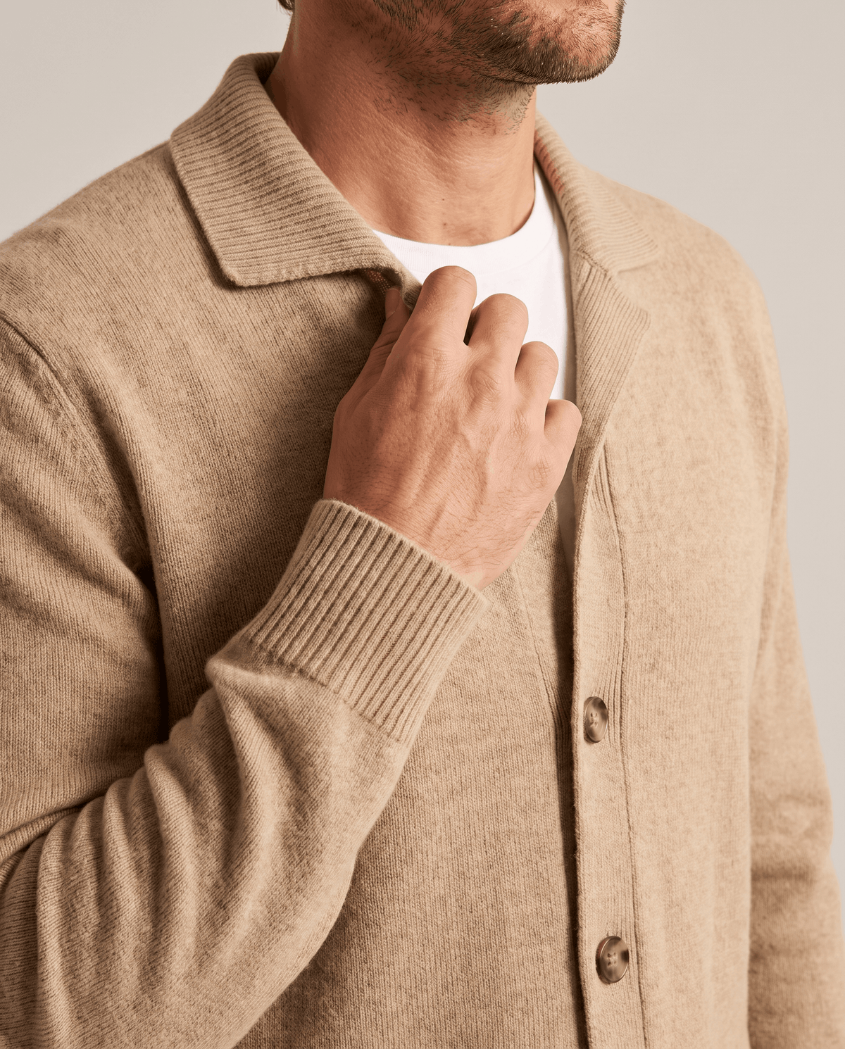 Hand at the shirt collar of a camel cardigan worn over a white tee