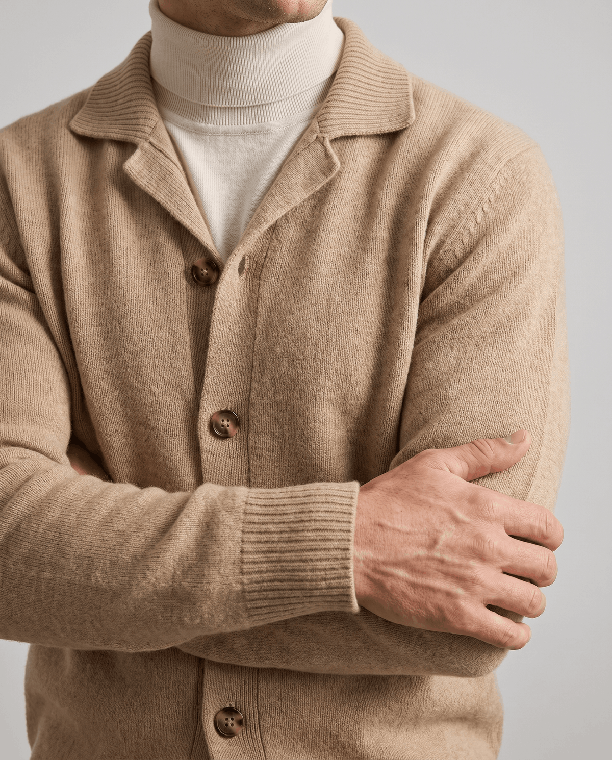 Arms crossed in a camel knit cardigan showing buttons and ribbed cuffs