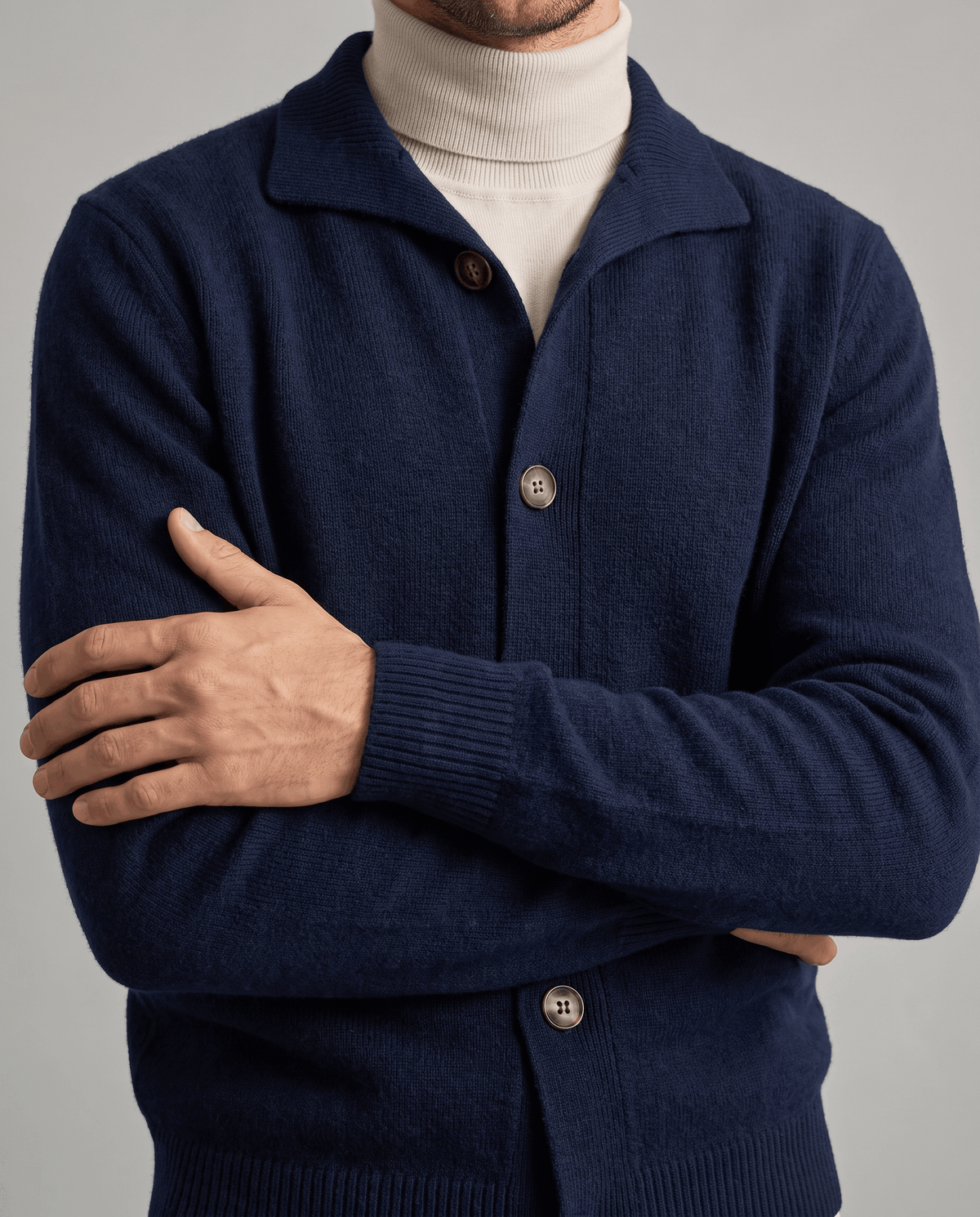 Arms crossed in a navy knit cardigan with a shirt collar over a cream turtleneck