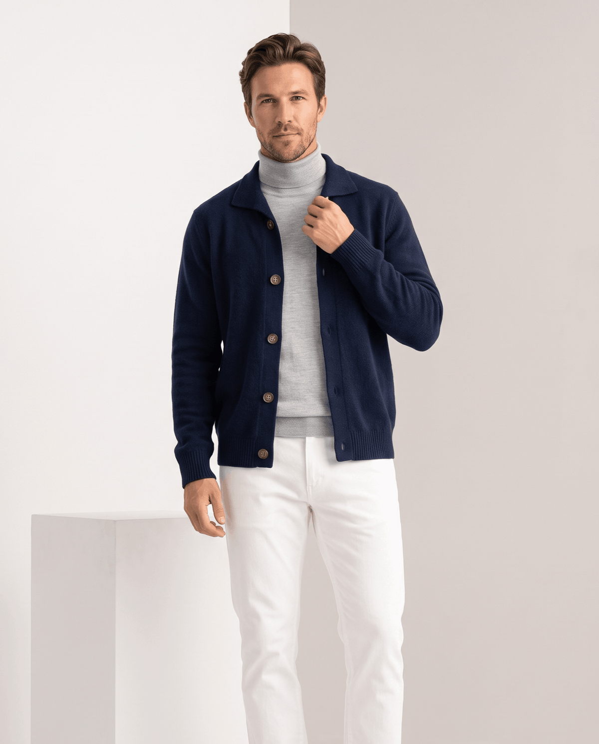 Navy collared cardigan worn open over a gray turtleneck with white trousers