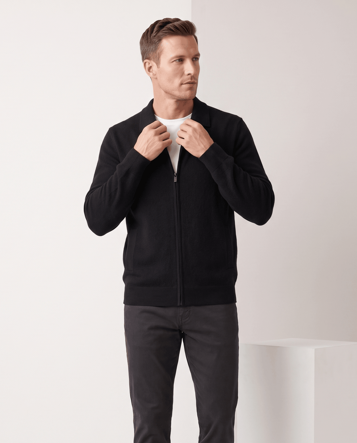 Man adjusting the collar of a black zip-up cardigan over a white tee
