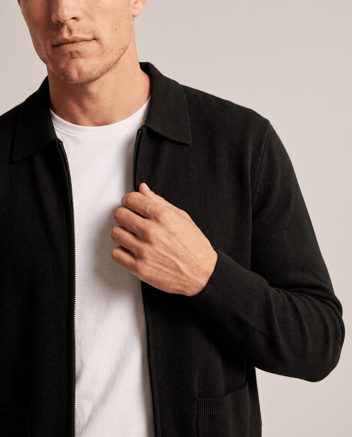 Hand on the zip of a black knit cardigan layered over a white tee
